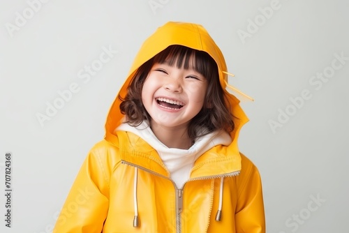 Happy little asian girl in yellow raincoat with hood over gray background