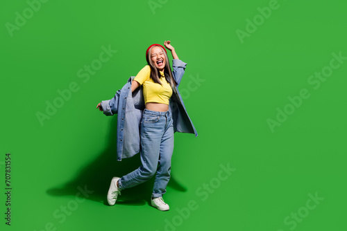 Full length photo of excited positive girl dressed jeans shirt dancing discotheque empty space isolated green color background