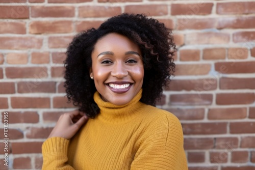 Curly African American woman wearing yellow shirt against red brick wall background