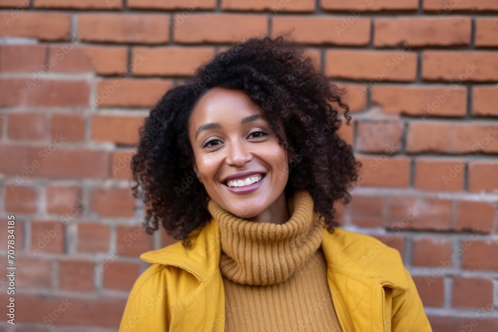Curly African American woman wearing yellow shirt against red brick wall background Curly African American woman wearing yellow shirt against red brick wall background