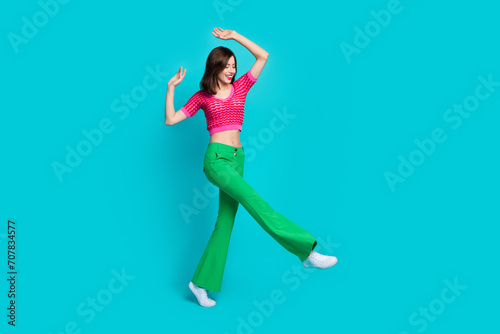 Full size photo of good mood nice girl wear pink top retro trousers dancing raising arms up at party isolated on blue color background