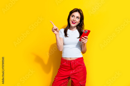 Portrait of attractive girl wear white t-shirt hold smartphone look directing at eshop empty space isolated on yellow color background photo