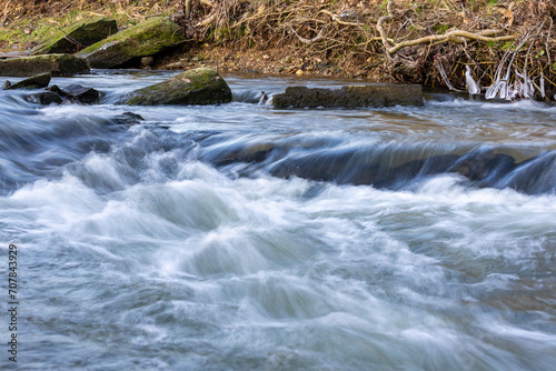 Water flowing quickly through a rapid of river Eschbach in Germany with waves, drops and splashes. Longtime exposure with motion
