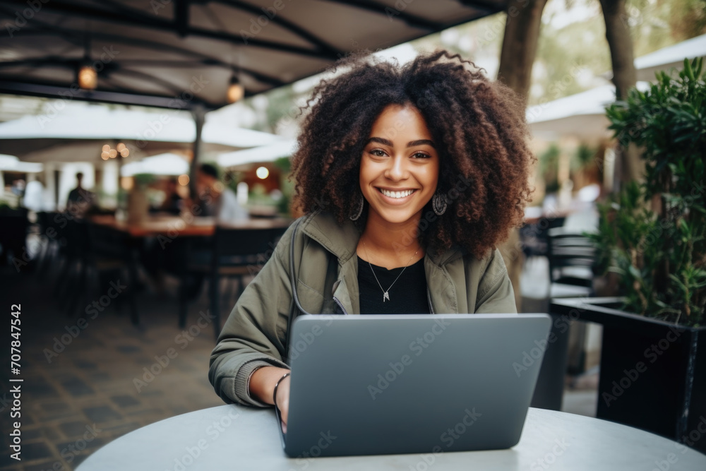 Cheerful young woman with curly hair using a laptop at an outdoor café. Cheerful young woman with curly hair using a laptop at an outdoor café.