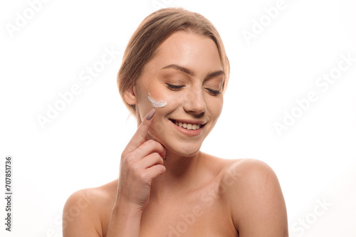 Beauty portrait of a beautiful woman applying cream on her face on an isolated white background. Skin care concept