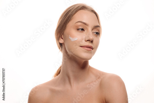 Beauty portrait of a beautiful woman applying cream on her face on an isolated white background. Skin care concept