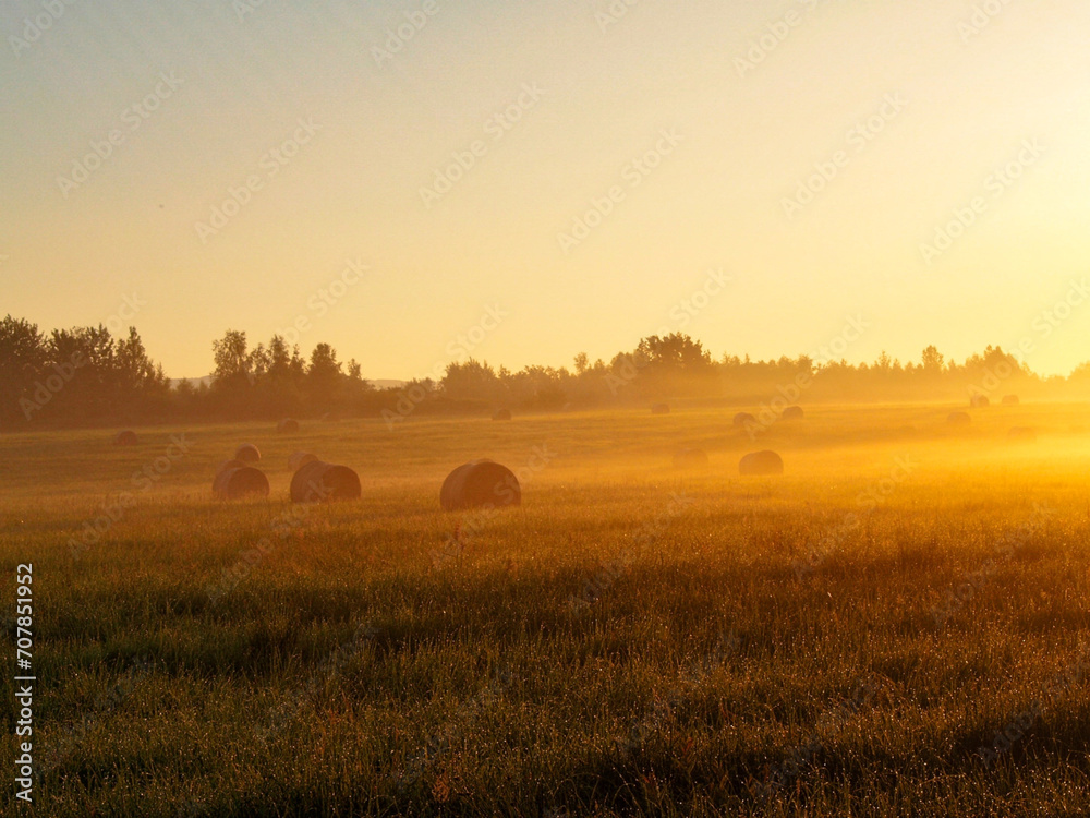 Sunrise in the field with bales of hay in the foreground