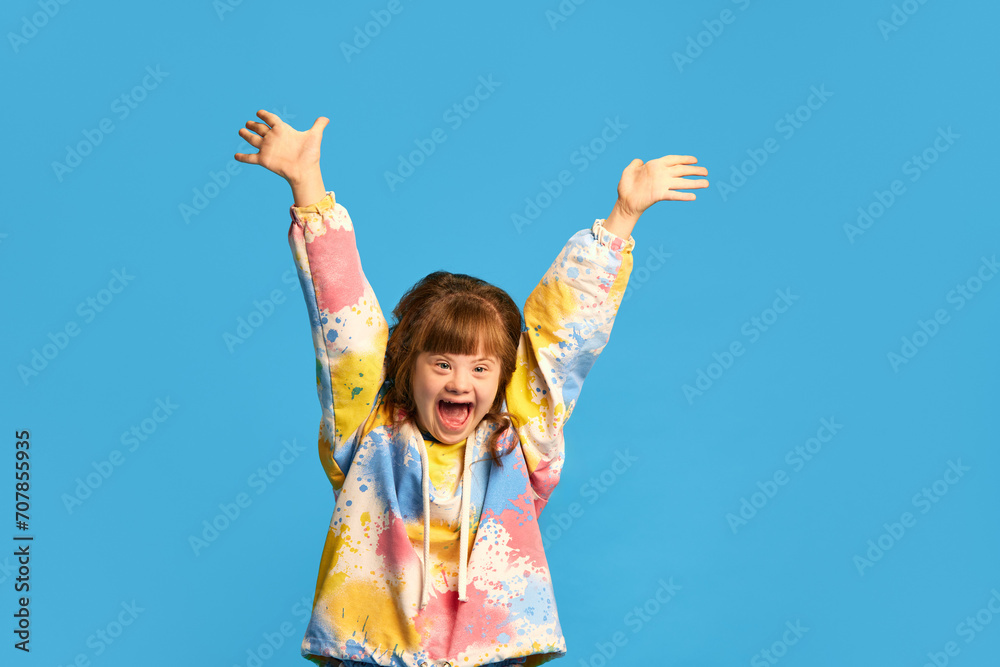 Careless and caring childhood. Happy smiling girl, child with down syndrome against blue studio background. Concept of acceptance, care, inclusion, health, diversity, emotions, therapy Careless and caring childhood. Happy smiling girl, child with down syndrome against blue studio background. Concept of acceptance, care, inclusion, health, diversity, emotions, therapy
