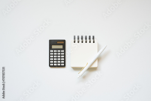 Black calculator, notepad, pen on white desk background. flat lay, top view