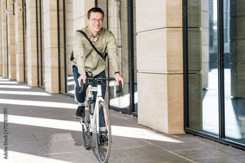 Smiling man cycling through city arcades, enjoying urban commute.