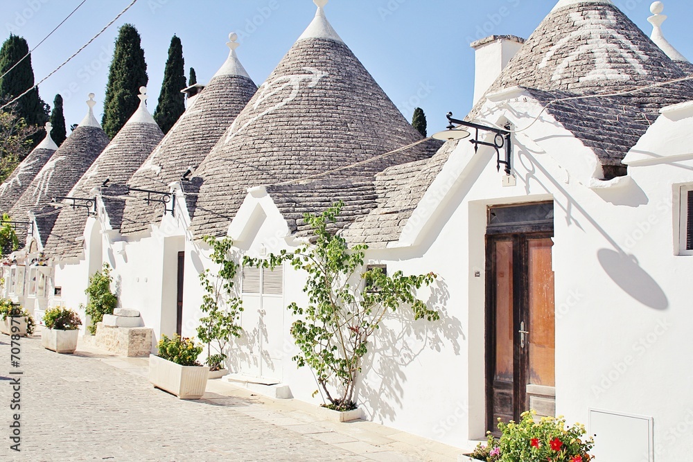 Fototapeta premium narrow street in an Italian town, white houses, white city, white stone buildings, the town of Alberobello, Italy, plants arranged next to the house