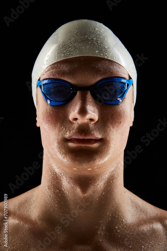 Portrait of young man, swimmer wearing goggles and swimming cap isolated over black background. Motivated swimming athlete. Poster for sport schools, events. Concept of competition, tournament