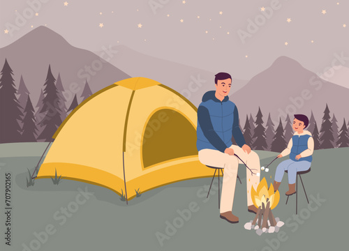 Smiling Father And His Little Son With Puffer Vest Sitting In Front Of Their Tent Roasting Marshmallows Over A Campfire. Full Length.