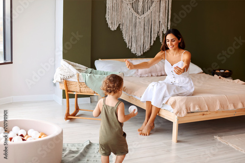 Young happy mother sitting on bed while her cute little boy son makig fisrt steps and learning to walk photo