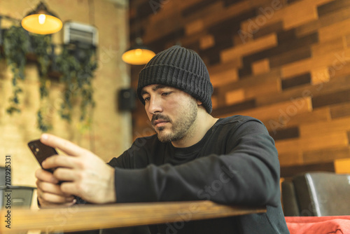 A man in a cafe drinks coffee and reads the news on the phone. Smiling and happy guy in cafe.