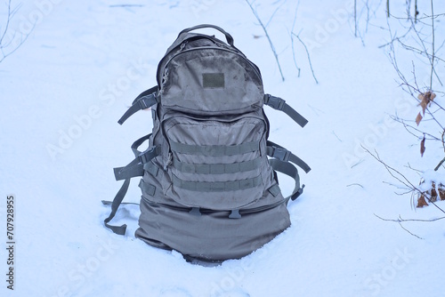 one large green army backpack stands on the ground and white snow in the winter forest