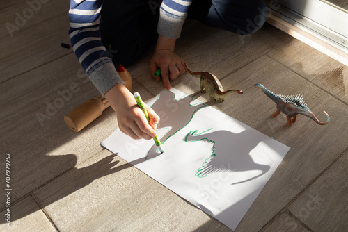 child draws contrasting shadows from toy dinosaurs on paper. ideas for children's creativity. Interesting activities for children at home and in kindergarten. View from above. little scientist