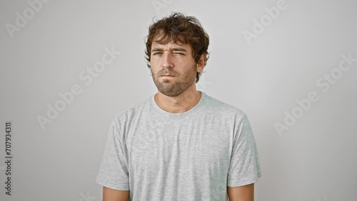 Nervous young man donning a casual t-shirt, expressing his displeasure with a skeptic frown etched on his face. deep in thought about his problem, he stands against an isolated white backdrop. photo