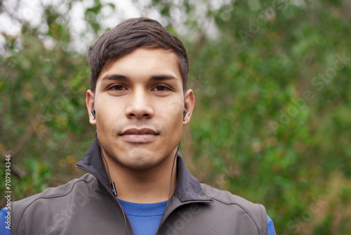 Earphones, runner or portrait of man in forest for workout, exercise or fitness training in park, woods or nature. Face, confident sports person or healthy athlete with radio music, wellness or audio