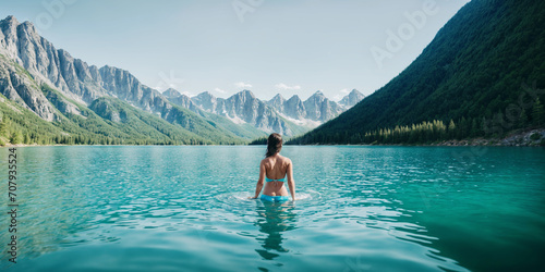 A woman enters the water of a mountain lake. Wild swimming, relaxing in mountain lake in nature, back view. 