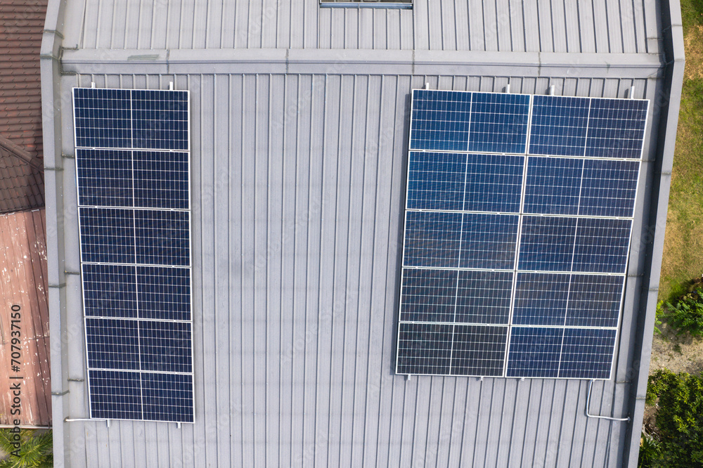 Top down aerial view of a large array of solar panels mounted on the corrugated metal roof of a house.