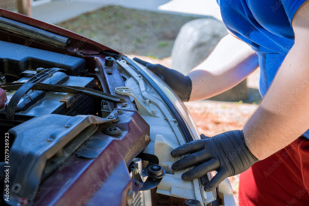 During car repair, mechanic assembles headlight on an automobile During car repair, mechanic assembles headlight on an automobile