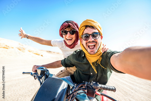 Young couple on a off road adventure excursion outside - Joyful tourists taking selfie with smart mobile phone in the desert - Tourism tour activities, transportation and summertime holidays concept photo