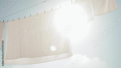 Slow motion. White, washed bed linen against a blue, sunny sky. The wind sways white linen against the backdrop of a bright sky. Washing, cleanliness, home, household, cleaning, housekeeping, fresh