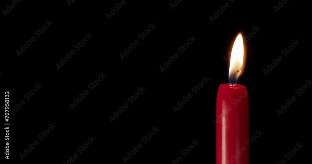 A single red candle burning. Isolated candle burning with dark background. Red paraffin candle with yellow shades burns on a black background. Background or illustration of remembrance or celebration. A single red candle burning. Isolated candle burning with dark background. Red paraffin candle with yellow shades burns on a black background. Background or illustration of remembrance or celebration.