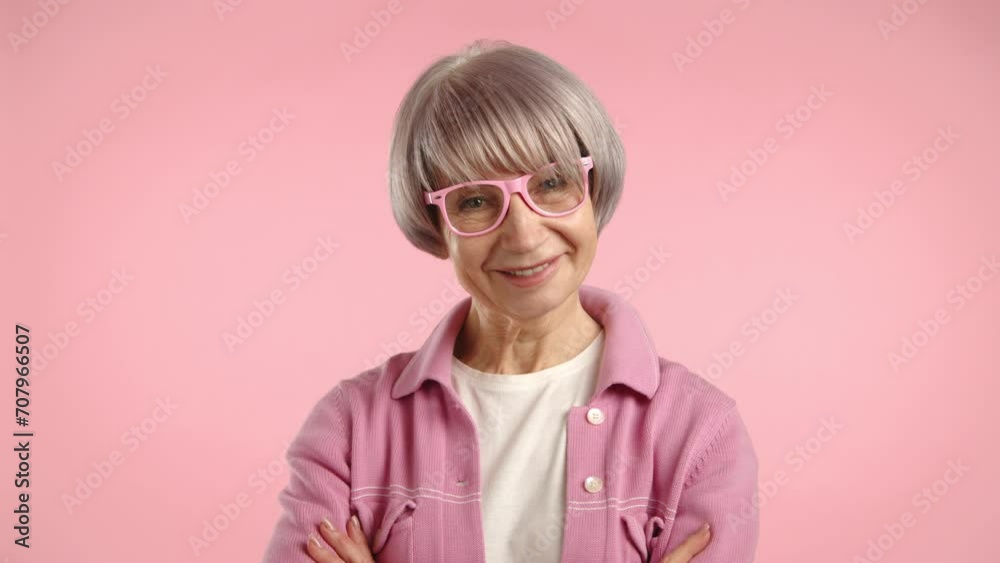 Stylish senior woman with silver hair smiling and adjusting her pink glasses. Wearing a soft pink jacket against a plain background. Camera 8K RAW Stylish senior woman with silver hair smiling and adjusting her pink glasses. Wearing a soft pink jacket against a plain background. Camera 8K RAW
