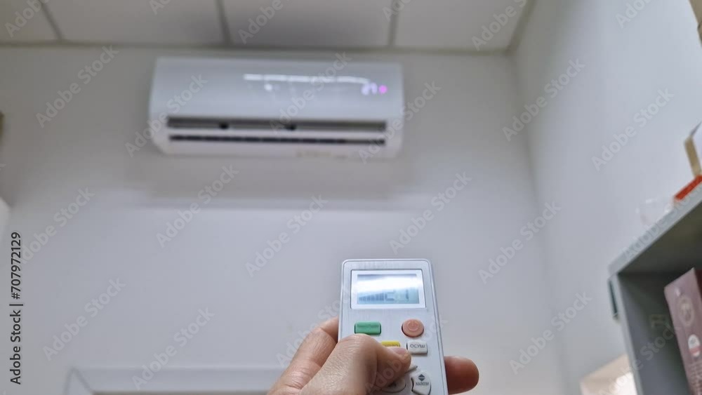 Closeup man hand holding a remote control to the air conditioning system pressing buttons as try to adjust the temperature in the room to a comfortable level. Home heating during cool season Closeup man hand holding a remote control to the air conditioning system pressing buttons as try to adjust the temperature in the room to a comfortable level. Home heating during cool season