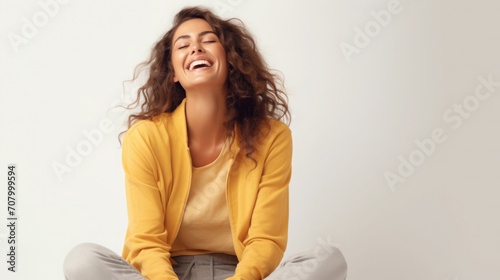 happy girl laughs, raising her head up, sitting in a yellow jacket, plain gray background