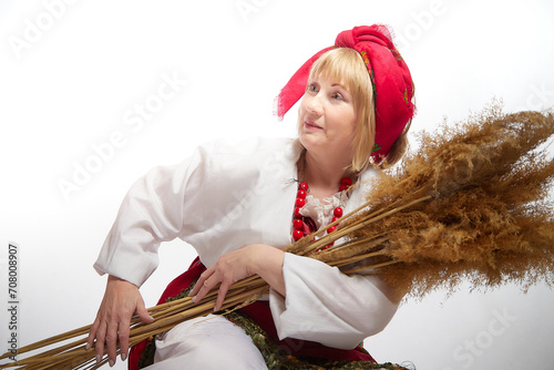 Portrait of heerful funny adult mature woman solokha with sheaf of ears. Female model in clothes of national ethnic Slavic style. Stylized Ukrainian, Belarusian or Russian woman in comic photo shoot photo