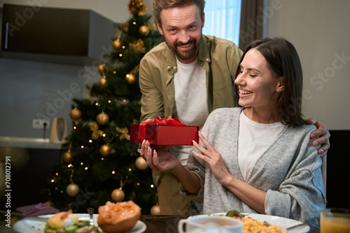 Happy man giving present to beautiful woman while having festive New Year dinner