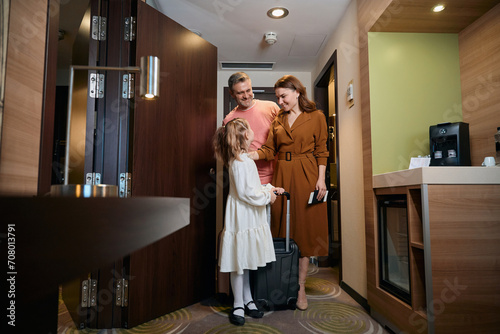 Family of mother, father and daughter with suitcase entering hotel room
