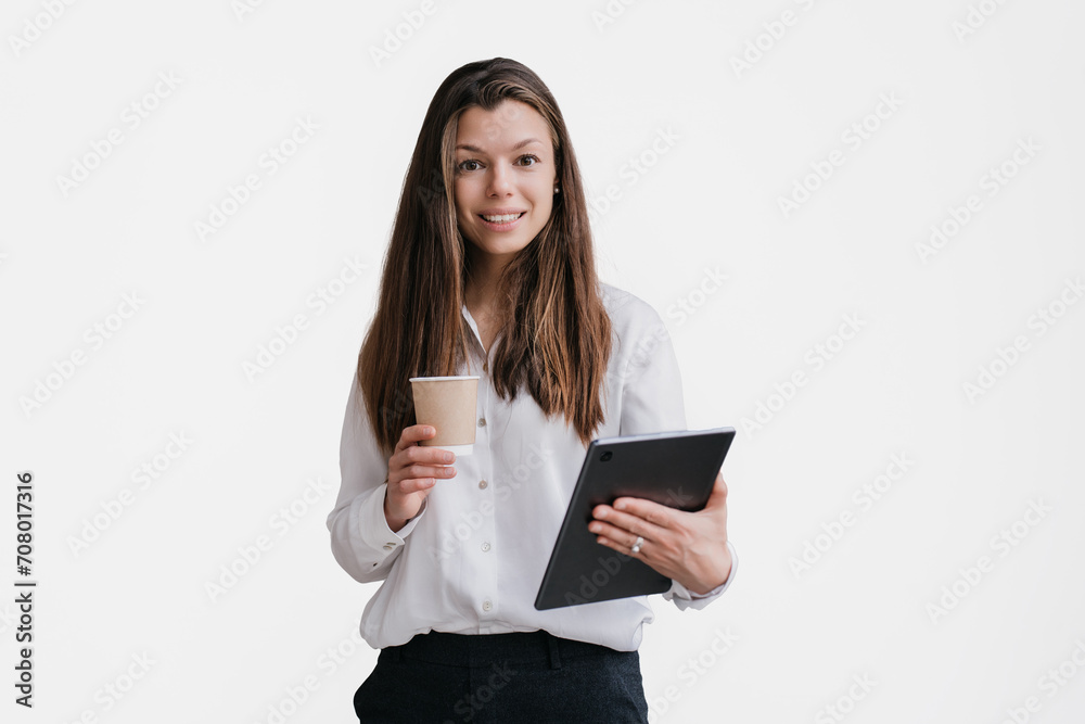 Young purposeful brunette businesswoman in white shirt and black pants holding tablet and cup of coffee looks at camera toothy smiles against transparent background. Smart student isolated Young purposeful brunette businesswoman in white shirt and black pants holding tablet and cup of coffee looks at camera toothy smiles against transparent background. Smart student isolated