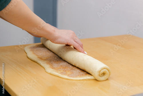One Caucasian young girl rolls cinnamon dough into a roll on the table.
