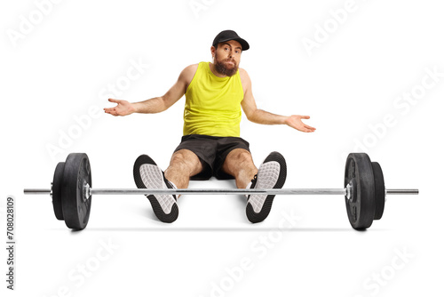 Confused man in sportswear sitting on the floor in front of a heavy barbell