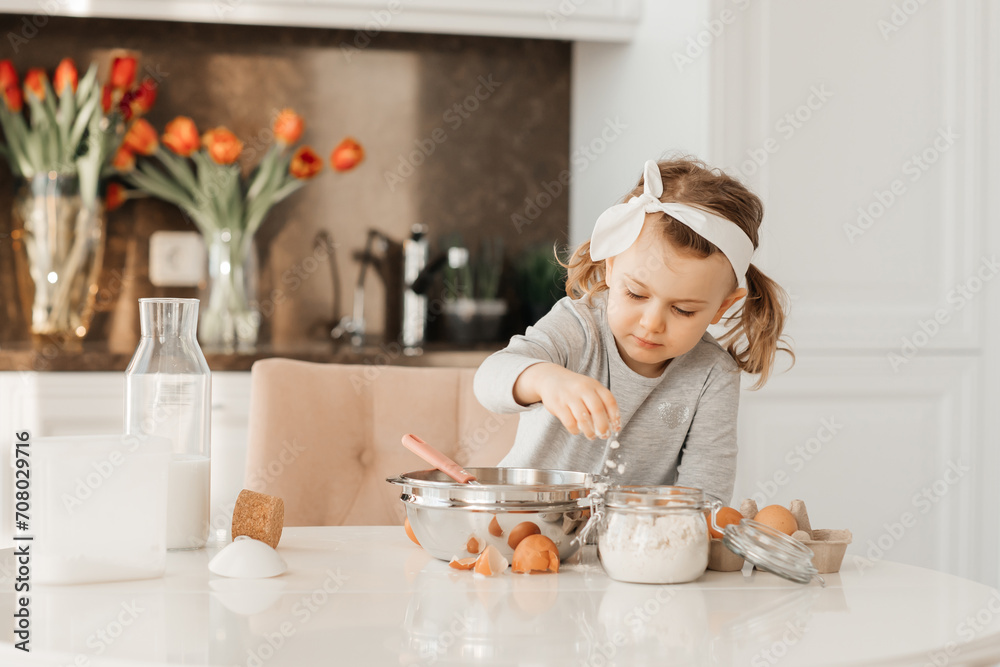 happy excited kid girl baking cake for Easter emotional child cook dessert present for mother day in white sunny kitchen Home bakery. Bottle of milk, eggs, flour are on the table