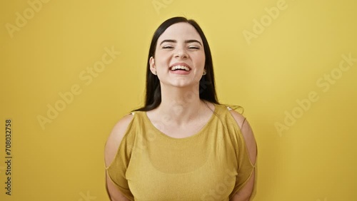 Hilarious shot of young, beautiful hispanic woman making a funny face, puffing up inflated cheeks catching air. standing person amused, eyes full of joy, against isolated yellow background. photo