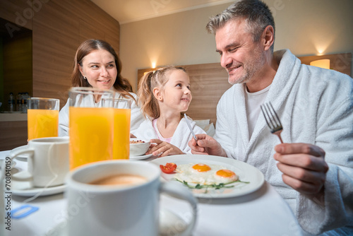 Mother and daughter looking at father during having breakfast in hotel room