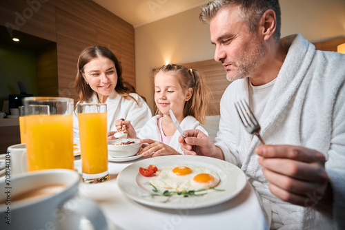 Mother and father looking at daughter eating flakes during having breakfast