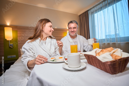 Couple having breakfast and looking at each other on bed at table in hotel room