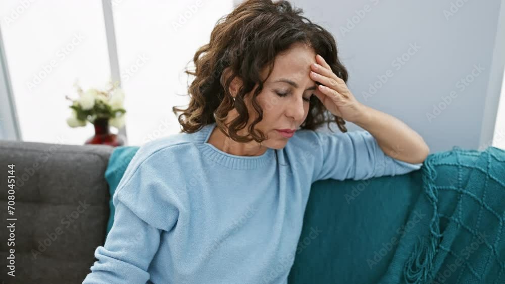 Mature woman with curly hair looking stressed in a cozy living room interior. Mature woman with curly hair looking stressed in a cozy living room interior.