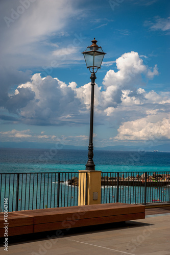 terrace above the sea with a street lamp, a bench and a dramatic sky