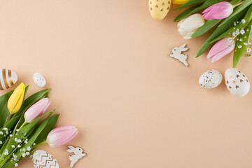 Crafting Easter celebrations. Top view composition of painted eggs, fresh tulips, cute easter bunnies on beige background with advert space