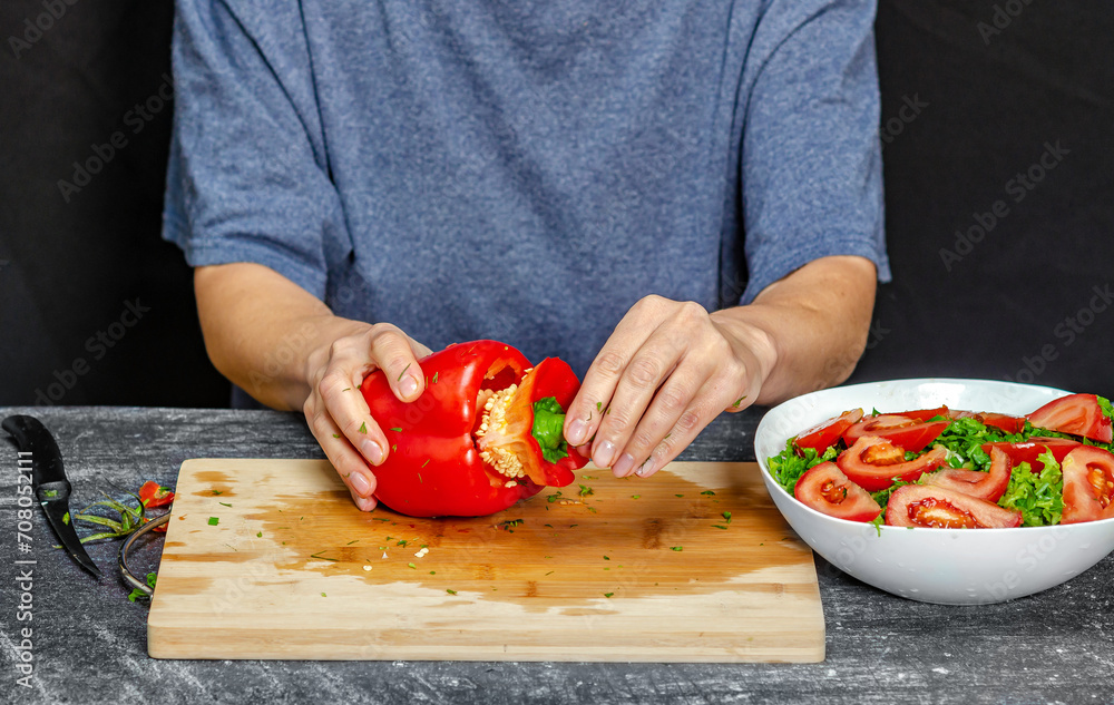 Female hands cutting pepper on cutting board. Blue t-shirt, black background. Salad preparation. Female hands cutting pepper on cutting board. Blue t-shirt, black background. Salad preparation.