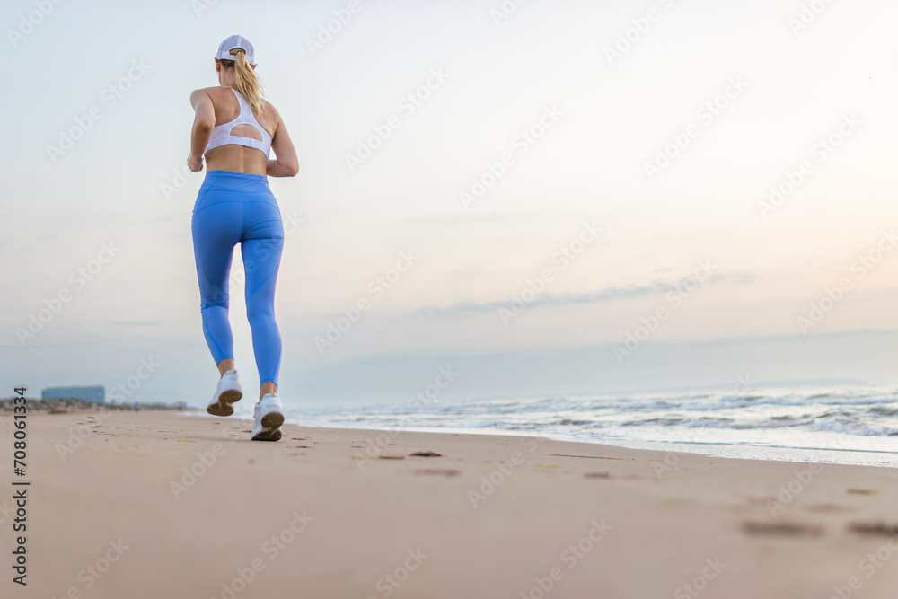 Beautiful sportive woman running along beautiful sandy beach enjoying active summer near the sea
