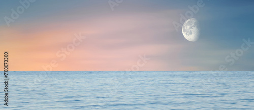 Wide sea view at sunset. Orange sun rays and moon in cloudless sky. Amazing landscape.