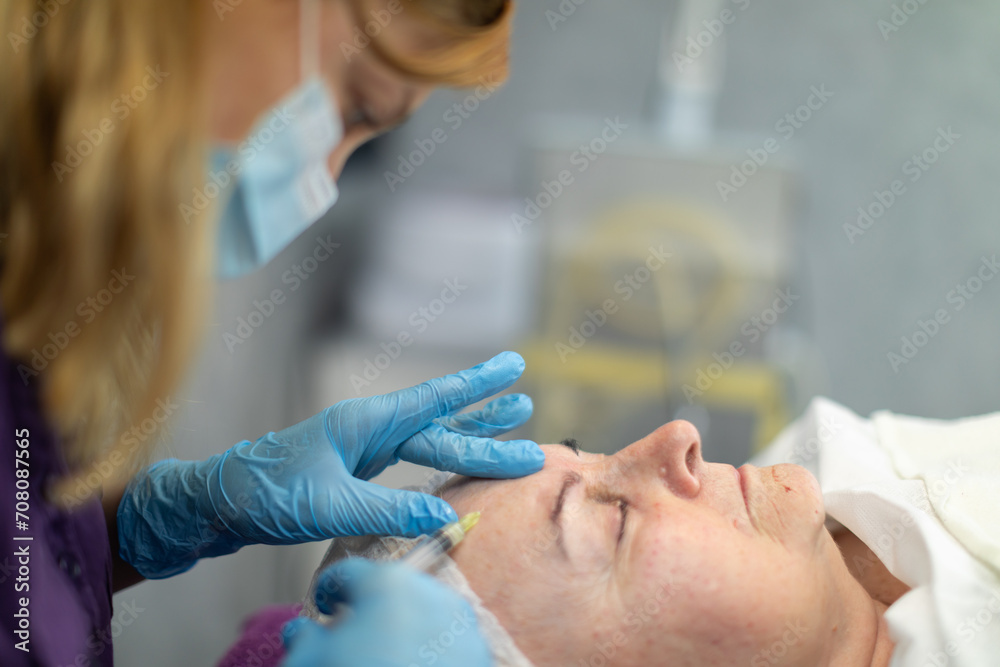 The beautician inserts a needle into the client's forehead to introduce the product under the skin. The beautician inserts a needle into the client's forehead to introduce the product under the skin.